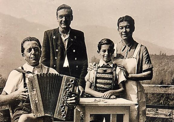 Schwarz-weiße Archivaufnahme der Gastgeber Familie gekleidet in Tracht mit einer Ziehharmonika