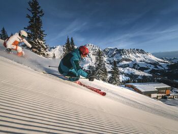 Zwei Skifahrer fahren auf einer frisch präparierten Skipiste im Sonnenschein im Skigebiet Mühlbach am Hochkönig