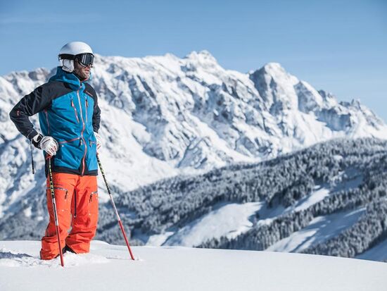 Ein Skitourengeher steht im Tiefschnee und schaut in die verschneite Landschaft vor einem Bergpanorama über das Gebirge des Hochkönigs