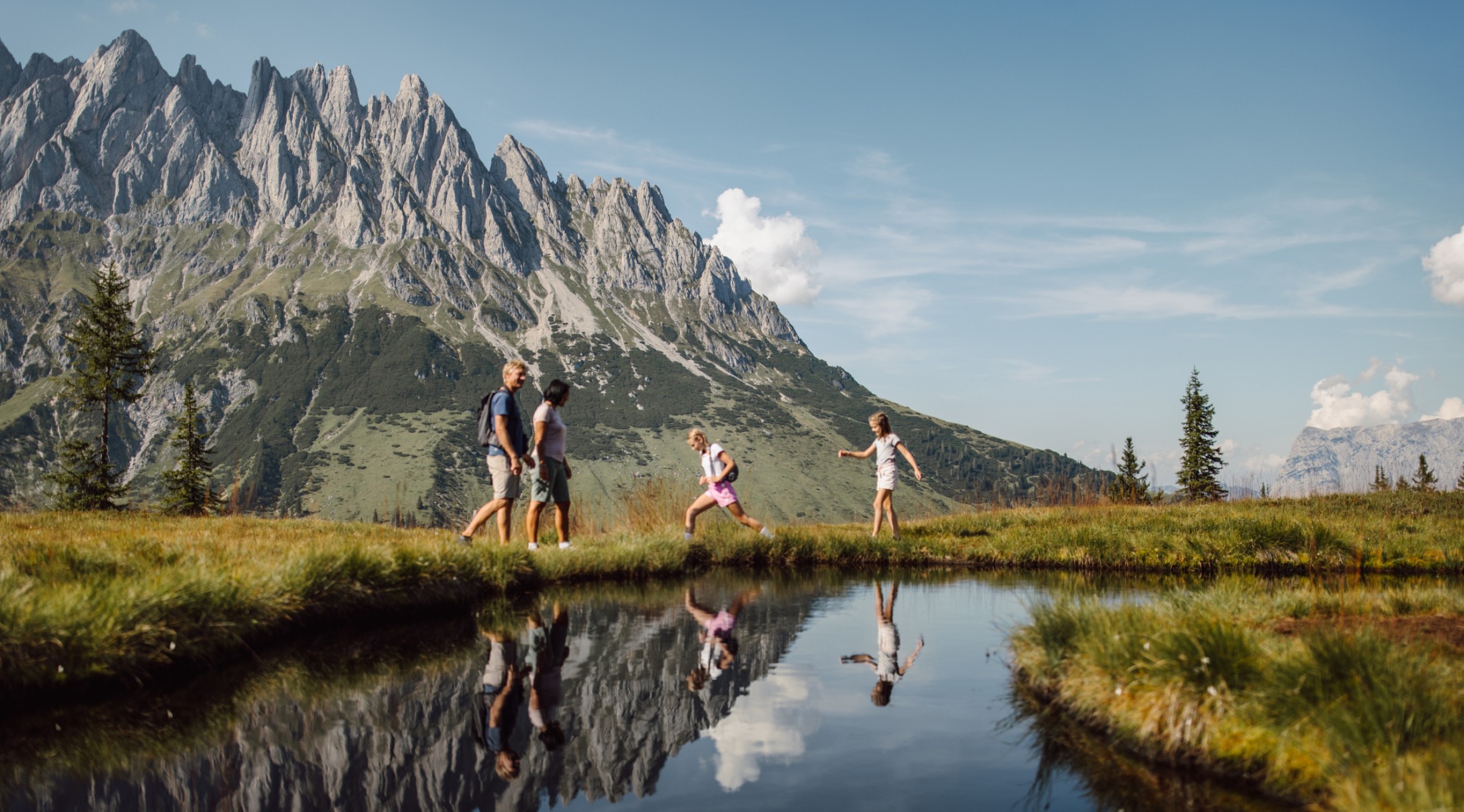 Familie beim Wandern entlang eines kleinen Bergsees mit Blick auf das Hochkönig-Massiv bei Mühlbach
