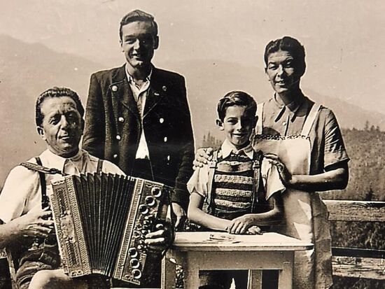 Schwarz-weiße Archivaufnahme der Gastgeber Familie gekleidet in Tracht mit einer Ziehharmonika