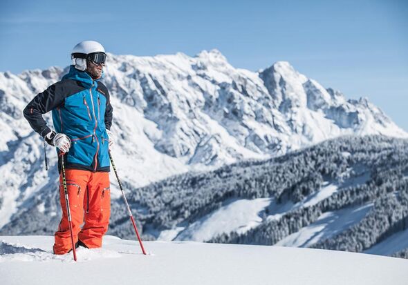 Ein Skitourengeher steht im Tiefschnee und schaut in die verschneite Landschaft vor einem Bergpanorama über das Gebirge des Hochkönigs