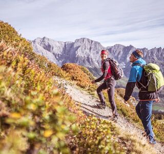 Eine Frau und ein Mann wandern im Sonnenschein auf einem Wanderpfad mit Ausblick auf das steinige Gebirge des Hochkönig Massivs in Salzburg